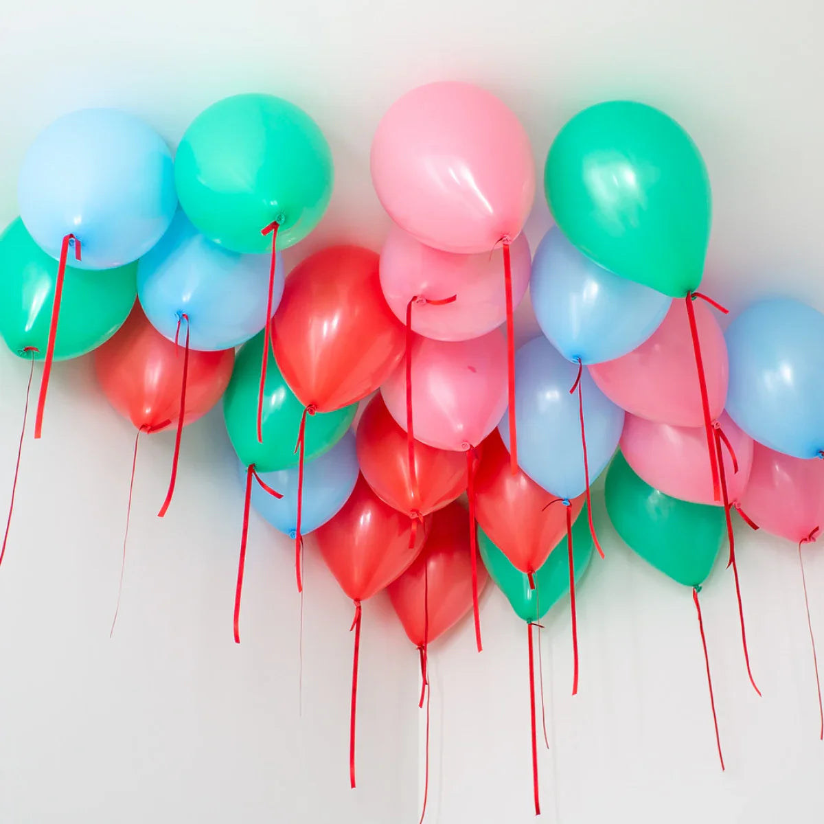 Colorful helium balloons in blue, green, pink, and red floating on ceiling with red ribbons