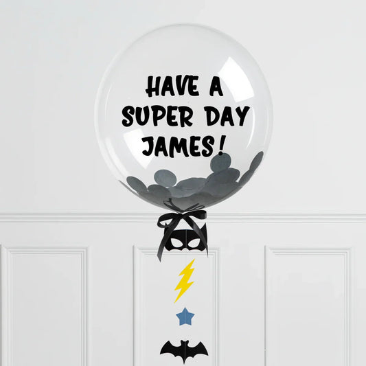 Clear personalized bubble balloon with black confetti and text 'Have a Super Day James!' with Batman-themed decorations