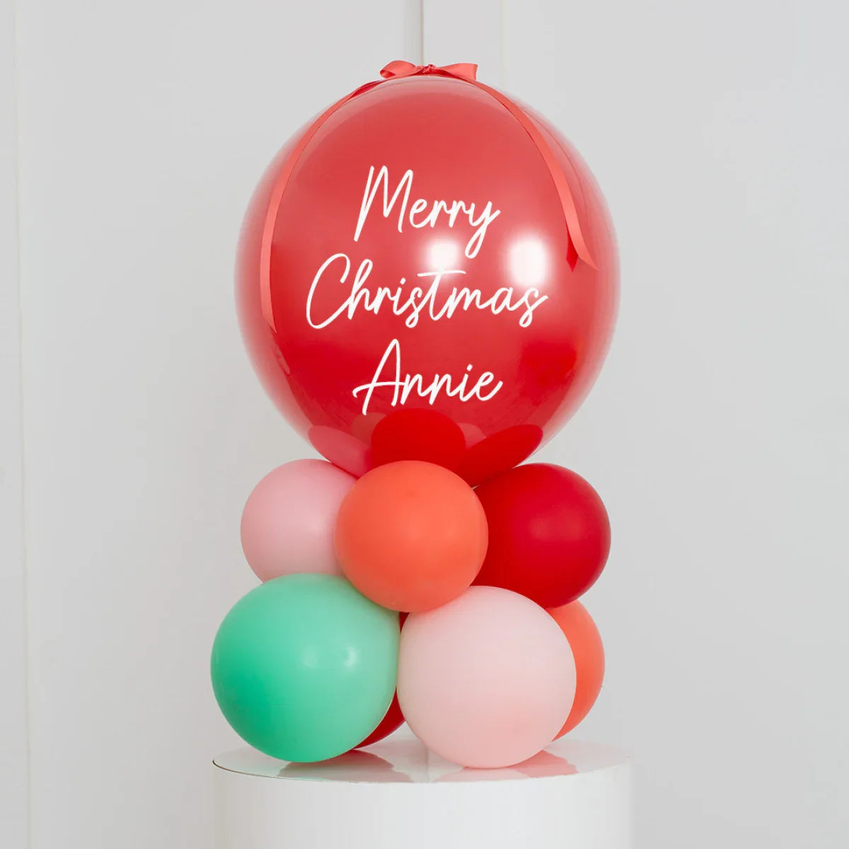 Personalized red Christmas balloon with "Merry Christmas Annie" text, surrounded by pastel pink, orange, and green balloons