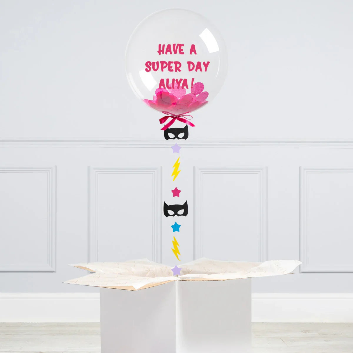 Clear bubble balloon with pink confetti and text Have a super day Aliya, floating above white box