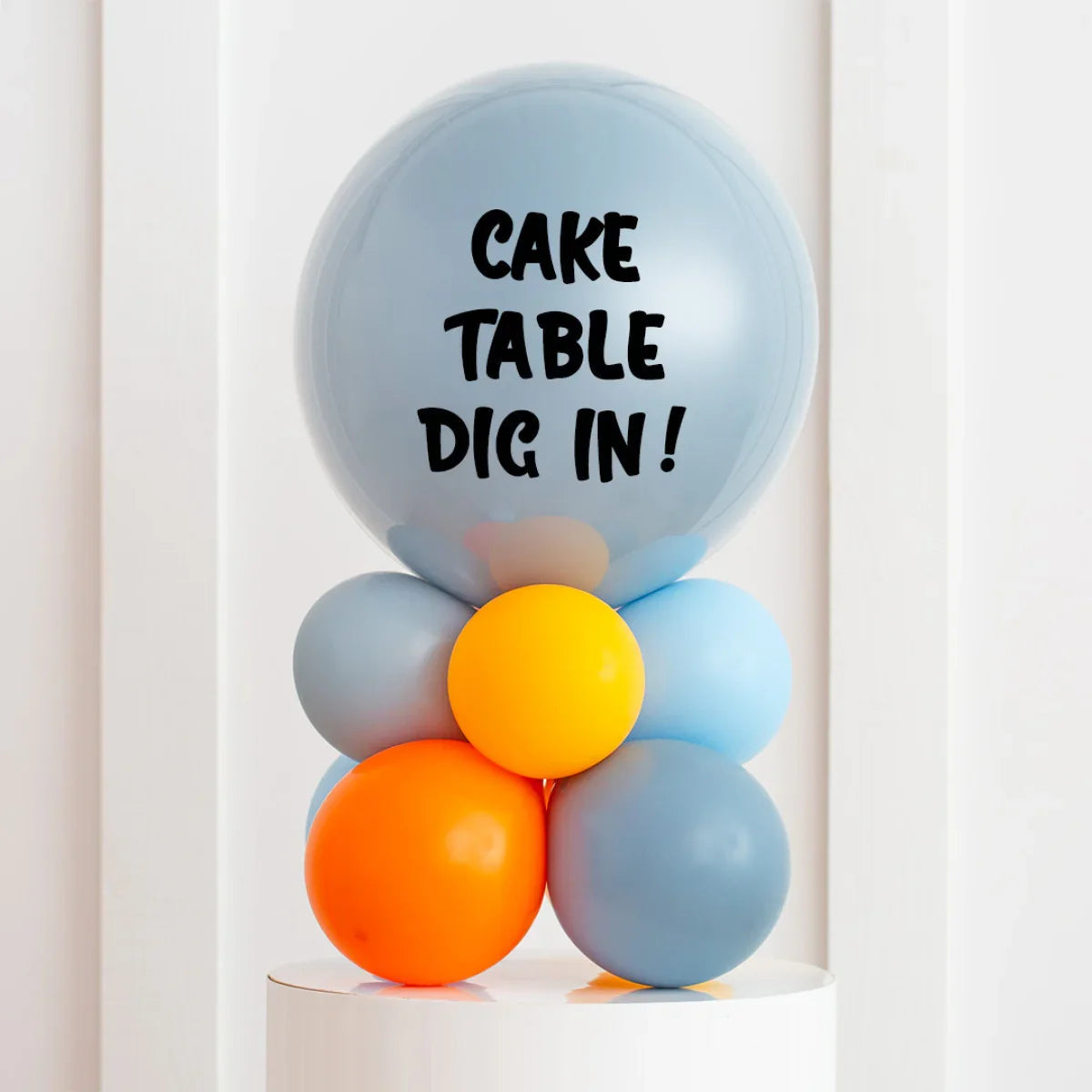 Colorful balloon stack with grey, orange, and yellow balloons and 'CAKE TABLE DIG IN!' text on top balloon