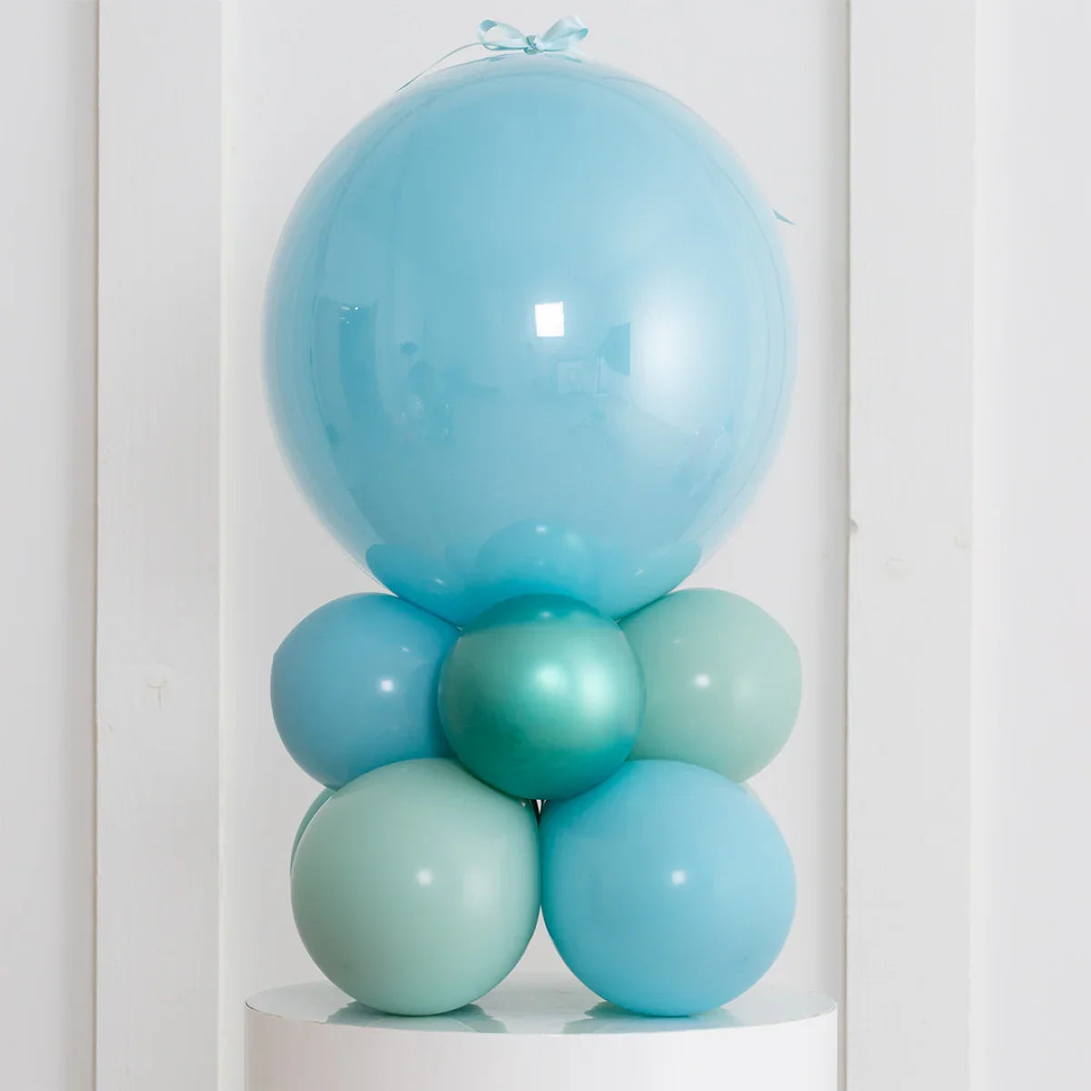 Personalised Blue Lagoon air-filled bubble balloon stack with pastel blue and teal balloons on white pedestal