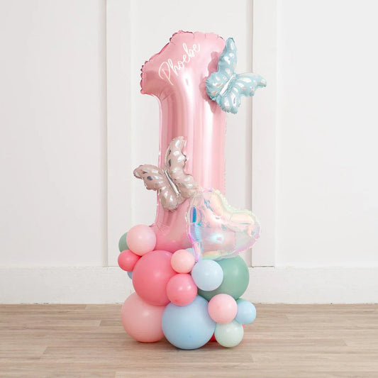 Pink number 1 balloon with personalized name and pastel butterfly and heart clusters on wooden floor