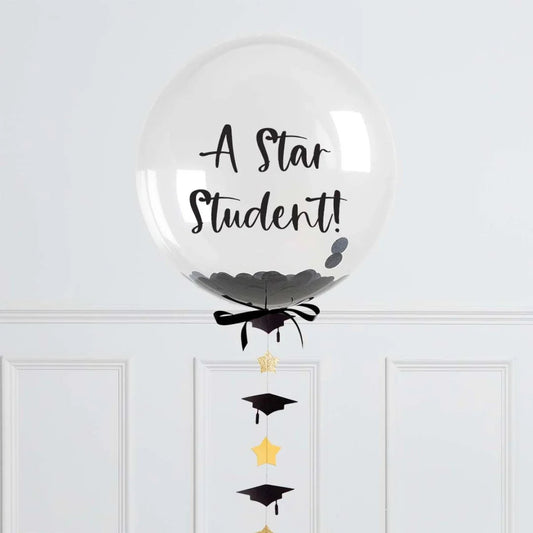Clear graduation balloon with black confetti, ribbon, and hanging gold stars and black caps