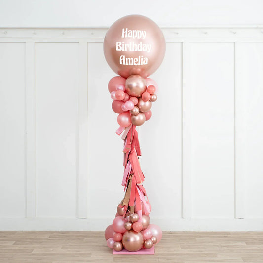 Rose gold and blush pink personalized birthday balloon pillar with Happy Birthday Amelia text