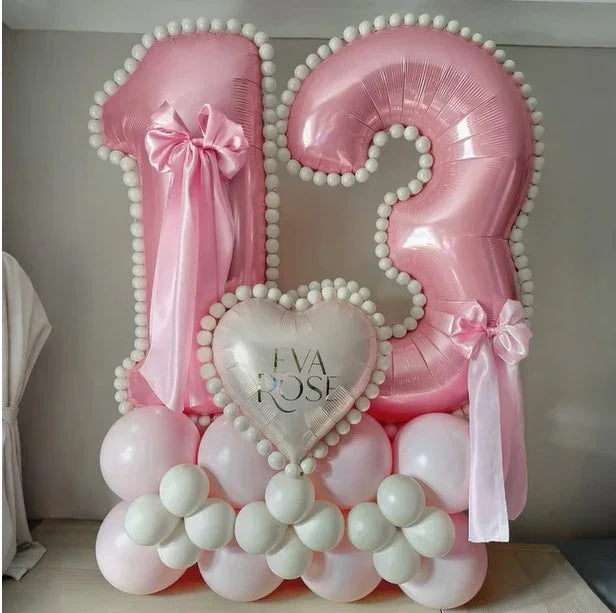 Pink number 13 balloon arrangement with white pom-pom trim, bows, and heart balloon saying Eva Rose