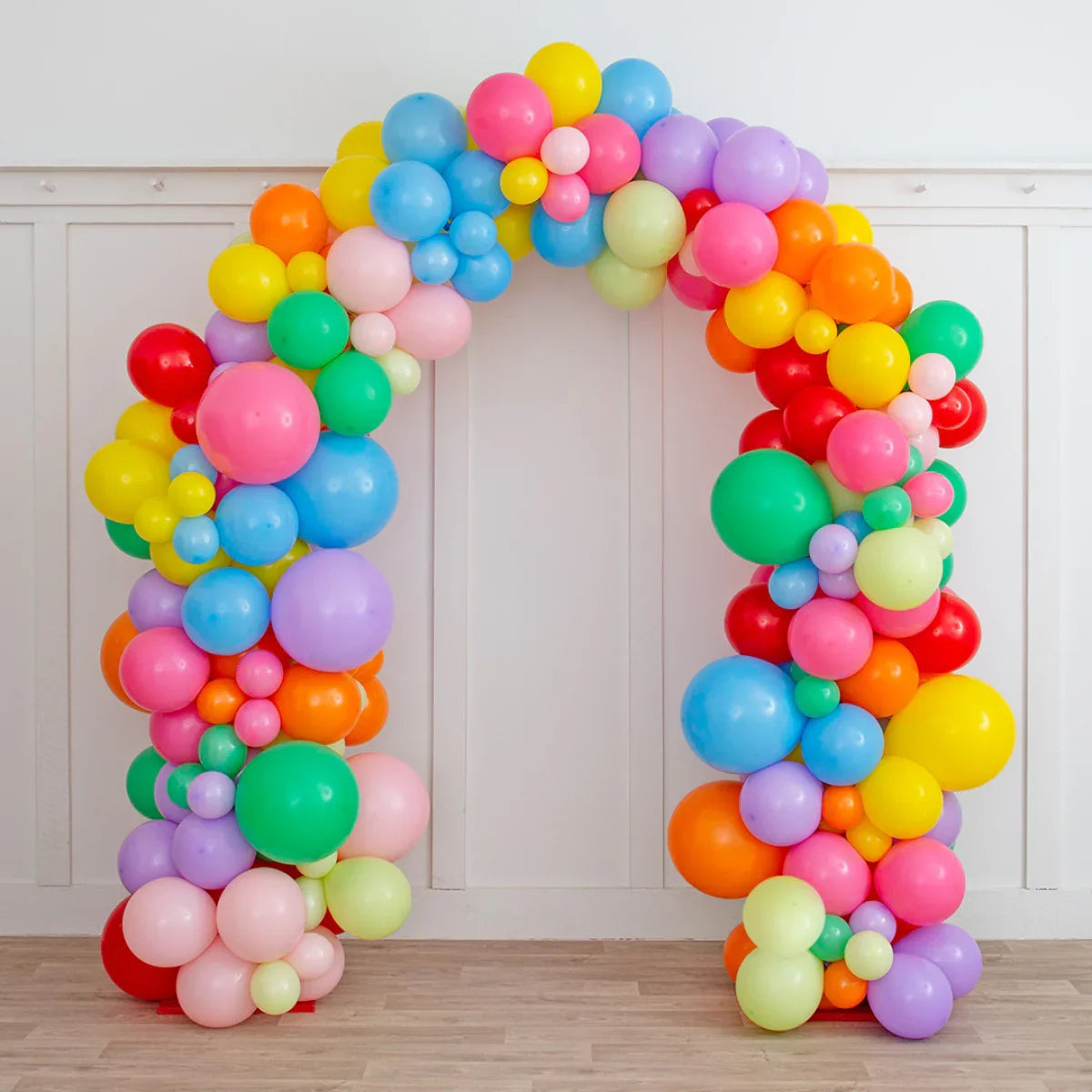 Colorful rainbow balloon arch with mixed sizes in indoor party setting on wooden floor