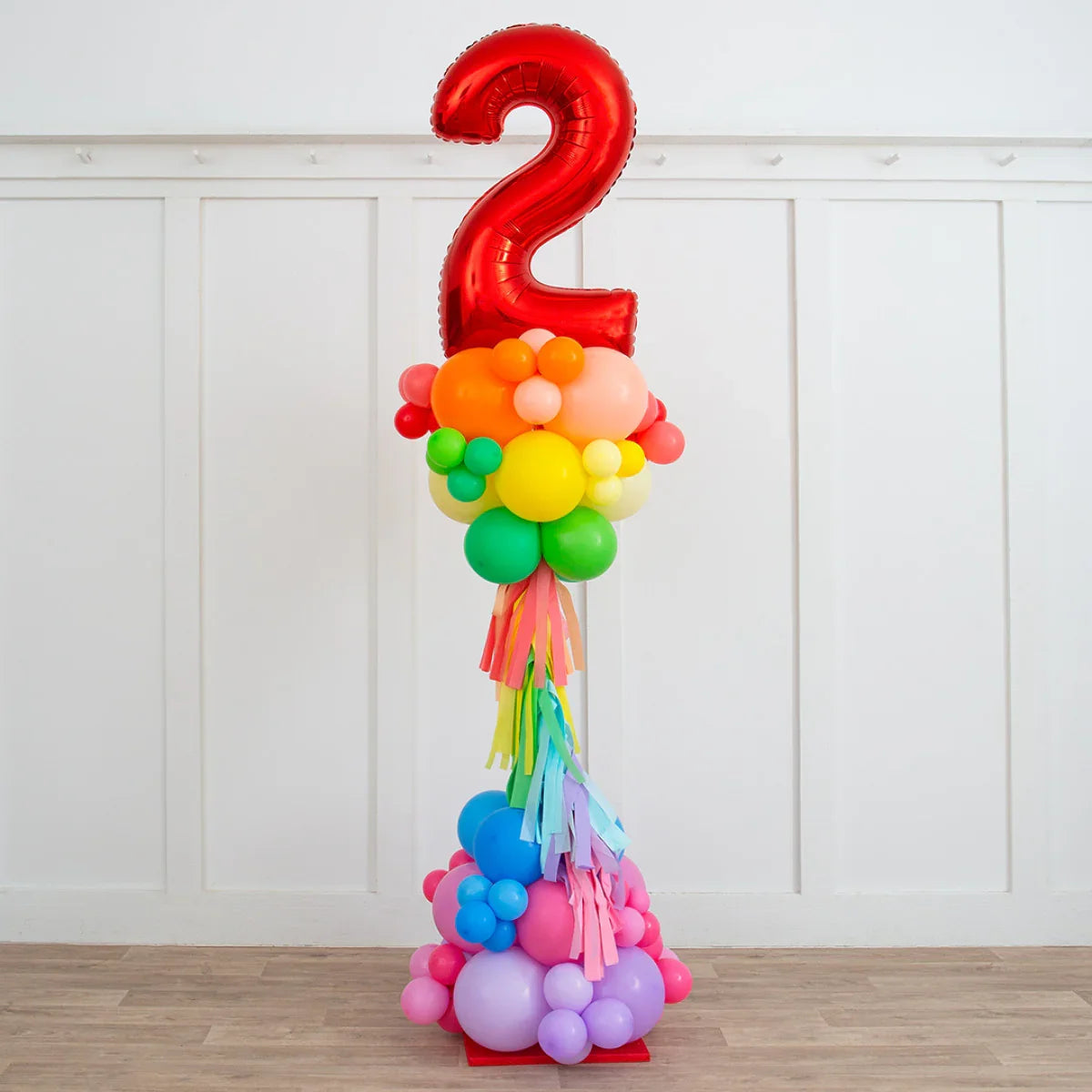 Colorful balloon pillar with large red number 2 balloon and rainbow fringe in a white room