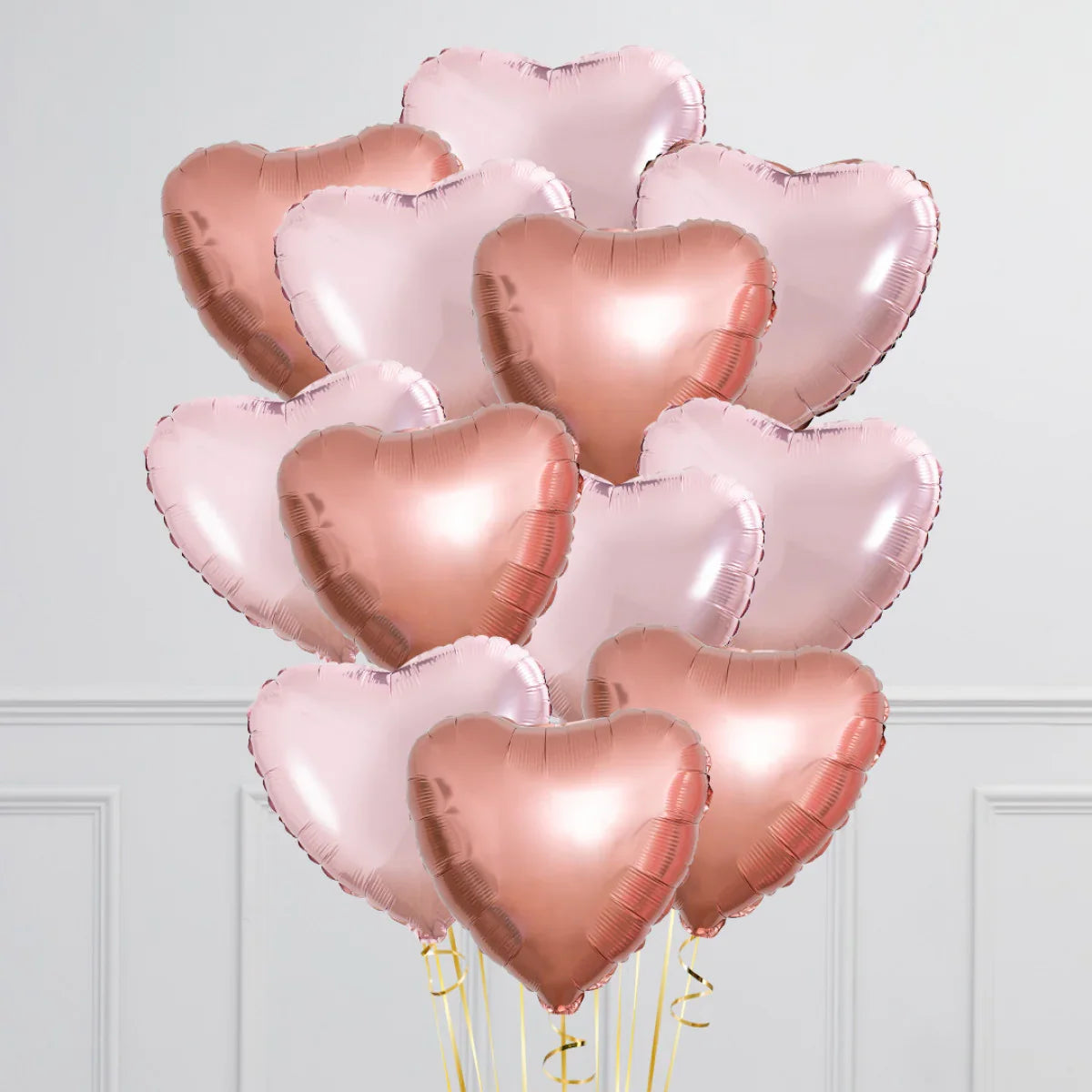 Cluster of rose gold and light pink heart-shaped foil balloons against white wall