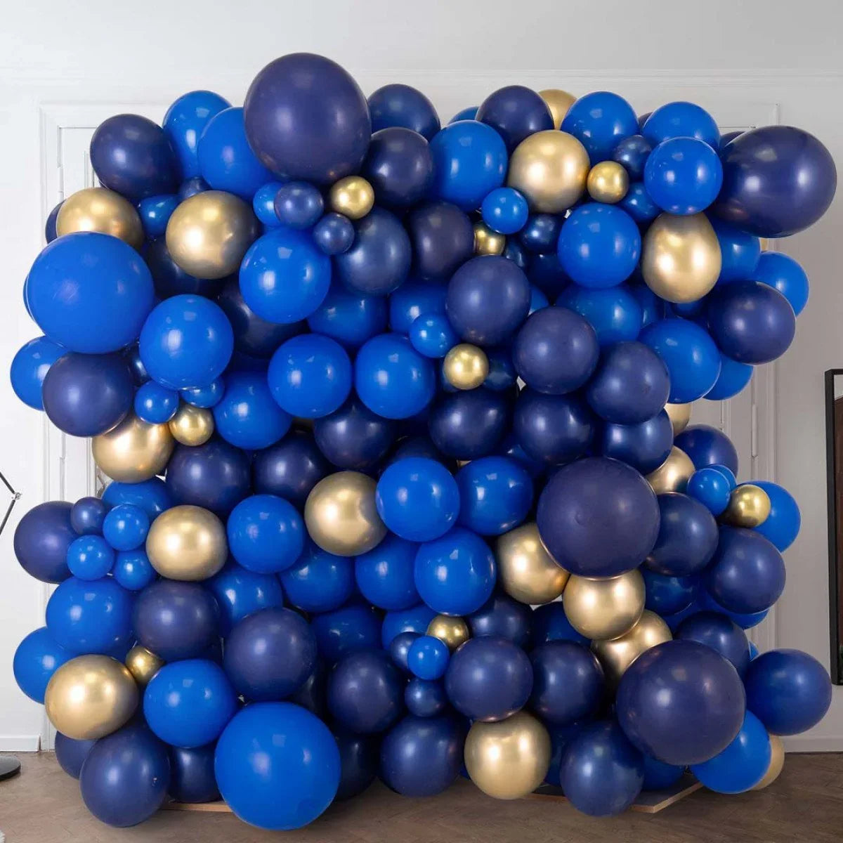 Large balloon wall decoration in sapphire blue, navy, and gold balloons indoors