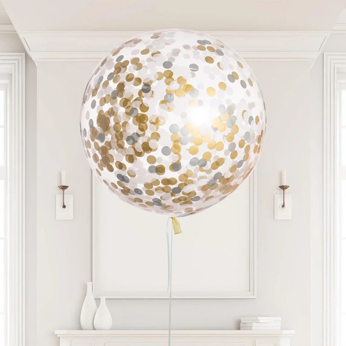 Large clear helium balloon filled with gold and silver confetti dots in a modern white room