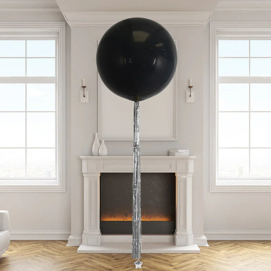 Large black helium giant balloon with metallic silver tassel tail in elegant living room with fireplace