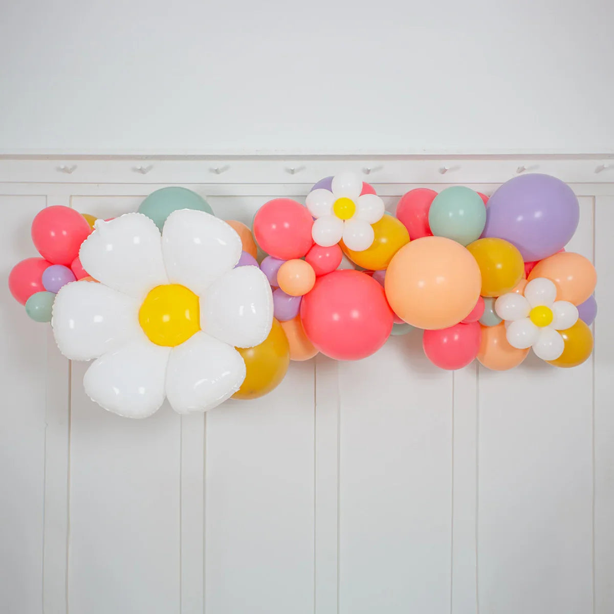 Colorful balloon garland with large white and small daisy-shaped flower balloons against white wall