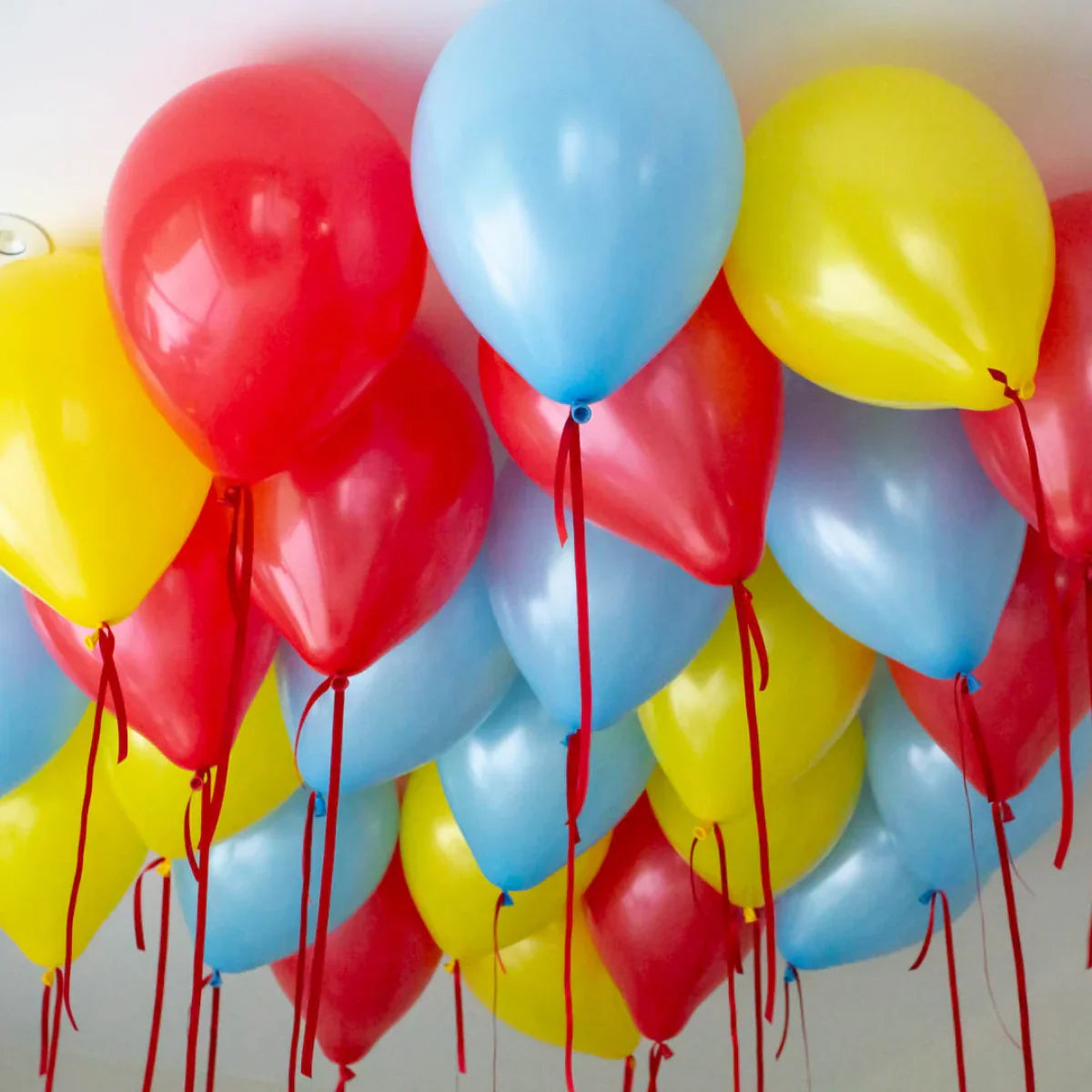 Cluster of red, yellow, and blue helium balloons floating on a ceiling with red ribbons