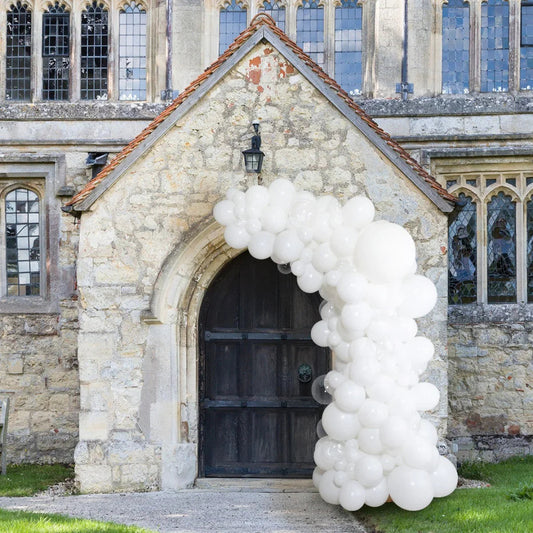 White asymmetric balloon arch decorating stone church entrance with dark wooden door and stained glass windows