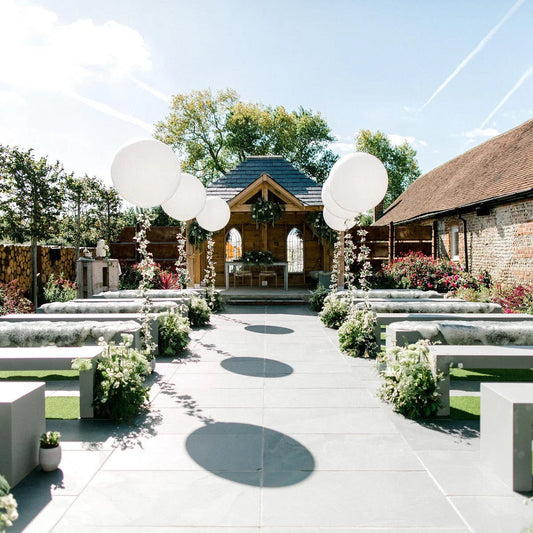Outdoor wedding venue with white giant balloons, floral decorations, benches, and a wooden gazebo