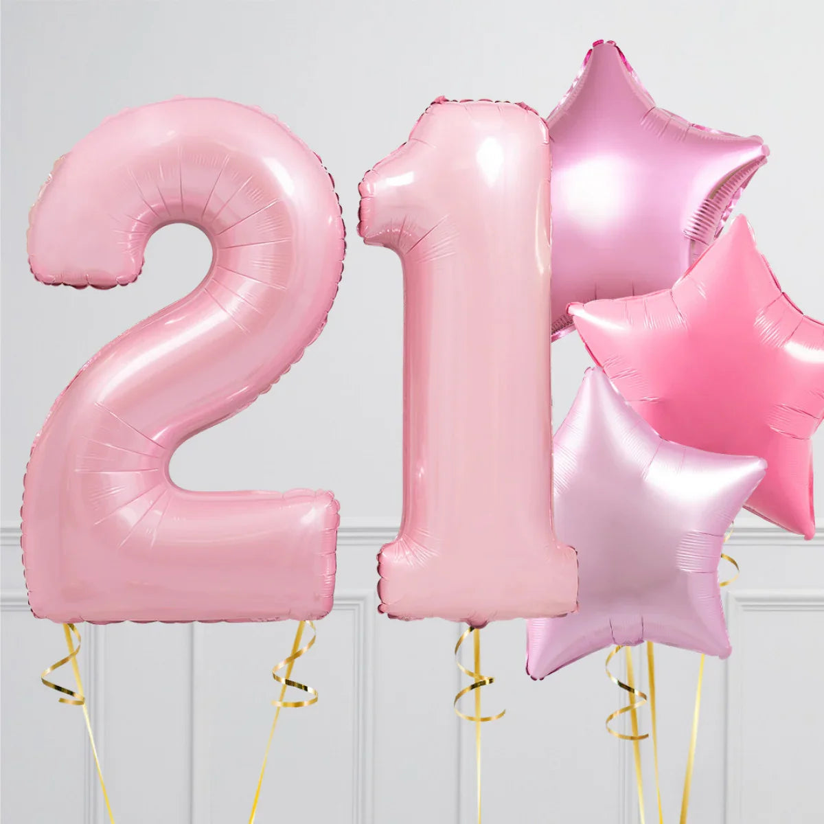 Pink foil balloons shaped as number 21 and four star-shaped balloons against a white paneled wall