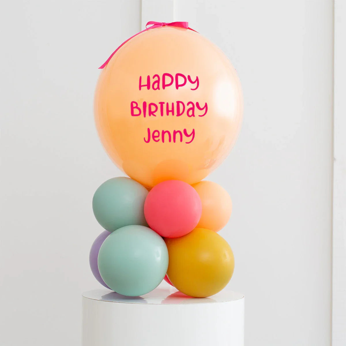 Personalised orange birthday balloon with message and colorful balloon cluster on white pedestal
