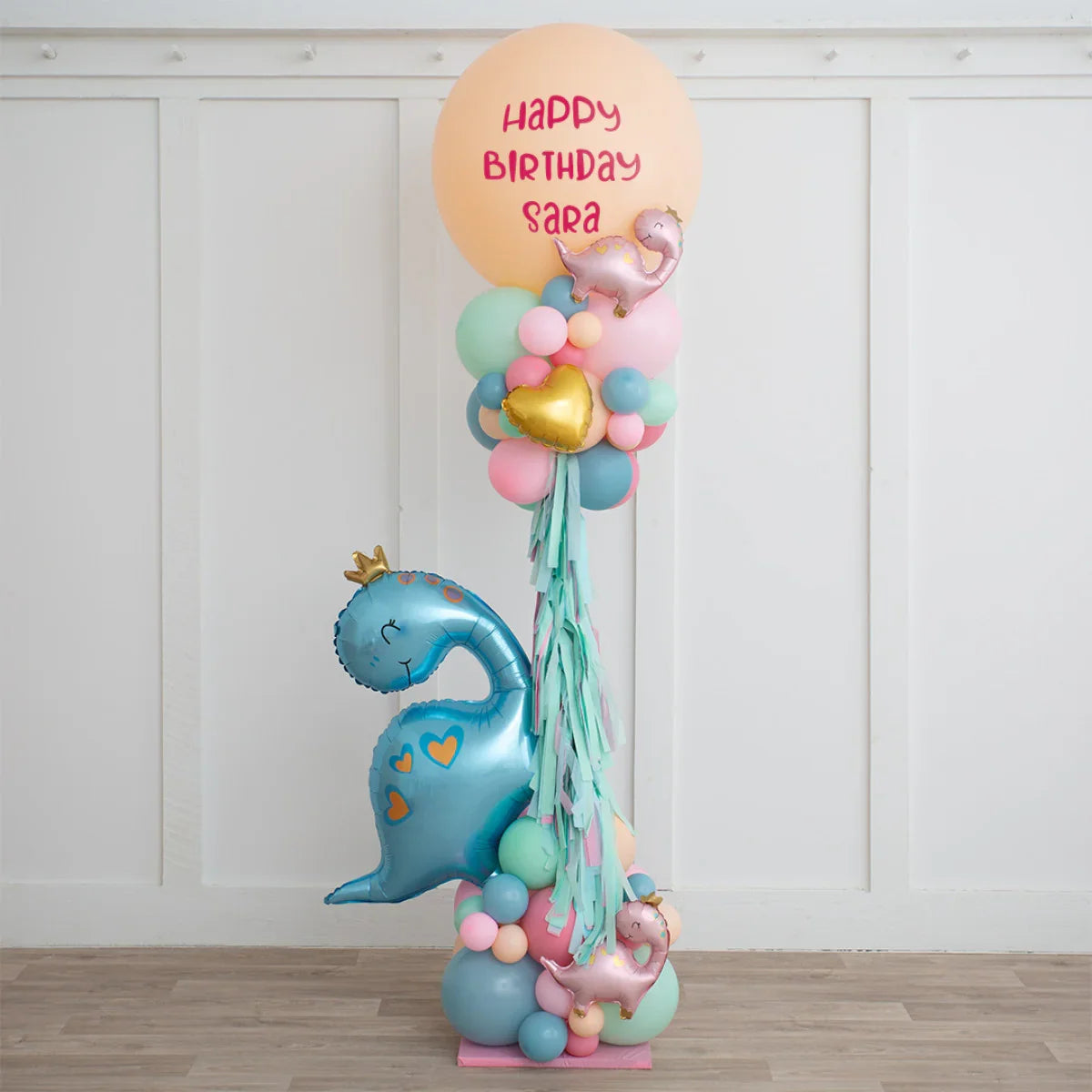 Dinosaur-themed birthday balloon arrangement with custom message Happy Birthday Sara in pastel colors