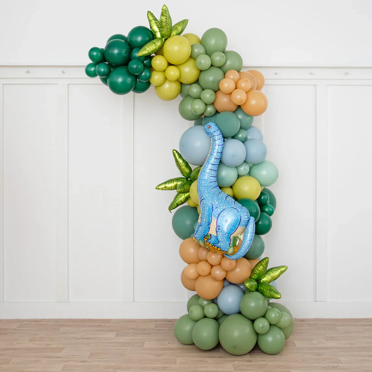 Dinosaur-themed balloon arch with green, blue, and brown balloons and a large blue dinosaur foil balloon