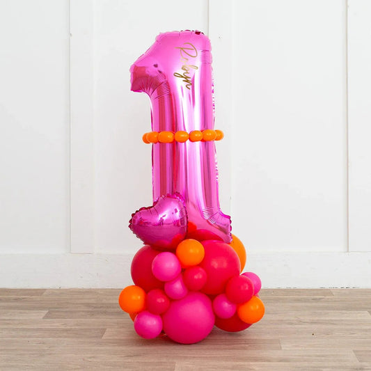 Pink foil balloon shaped as number 1 with orange and pink round balloons decoration on wood floor against white wall