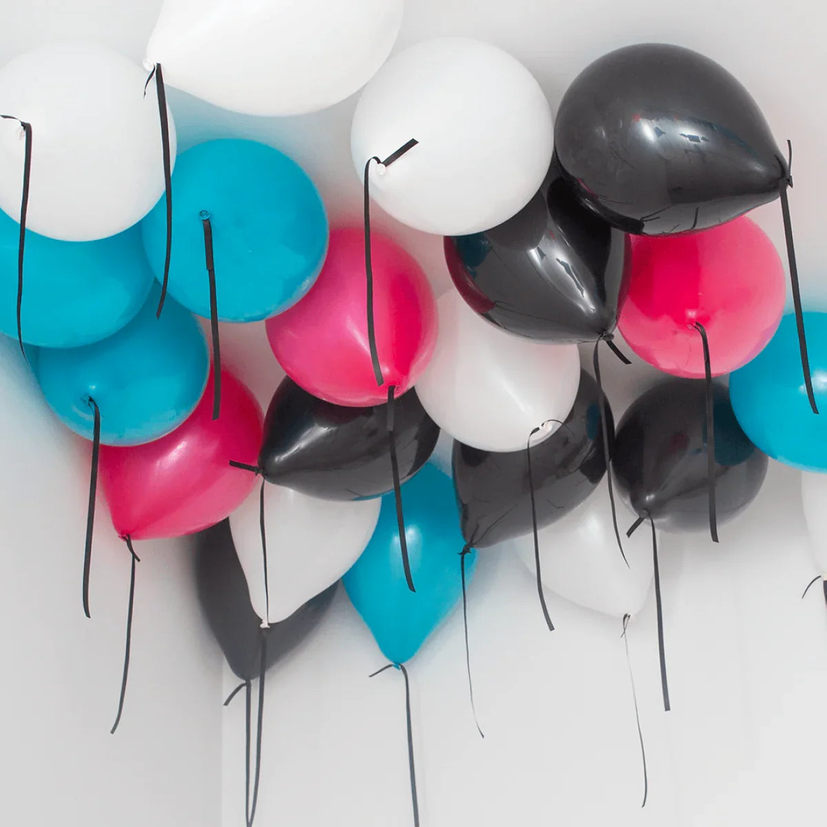 Helium-filled balloons in black, white, blue, and pink clustered on a white ceiling corner