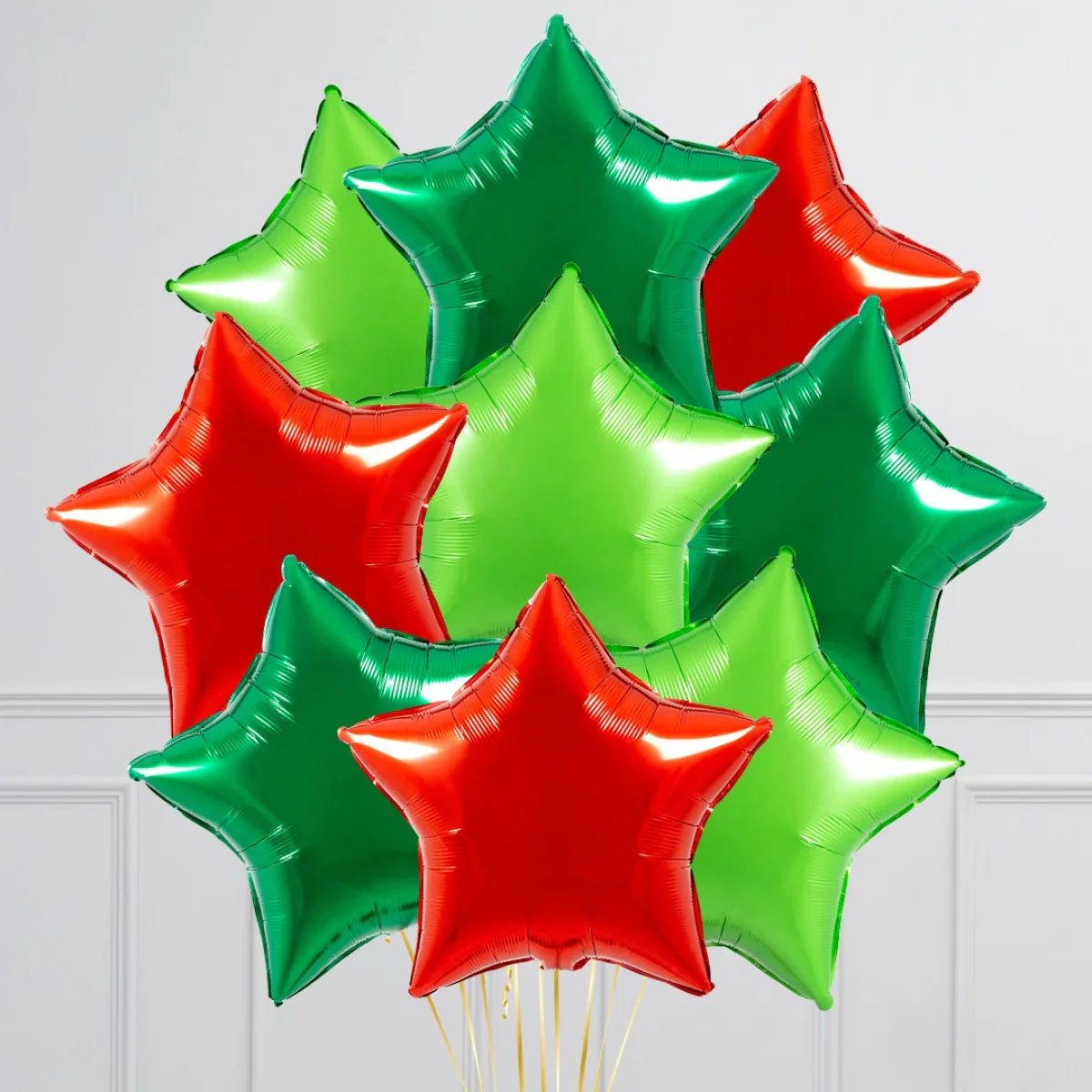 Cluster of shiny red and green star-shaped foil balloons against white wall background