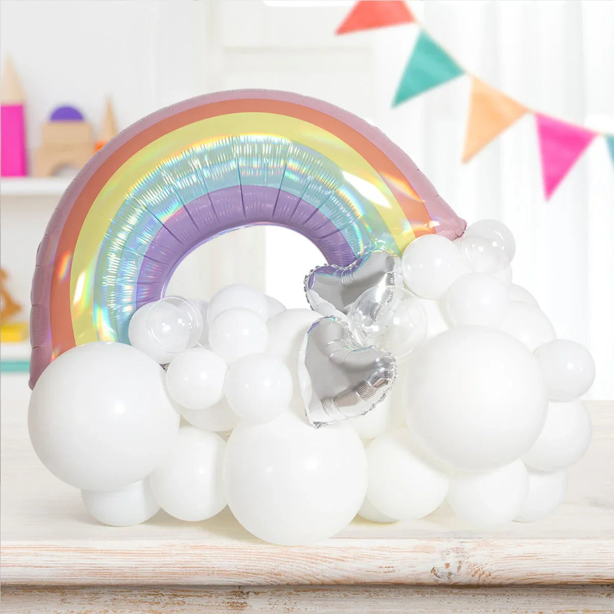 Pastel rainbow-shaped balloon with white and silver heart balloons on a wooden surface in a decorated room