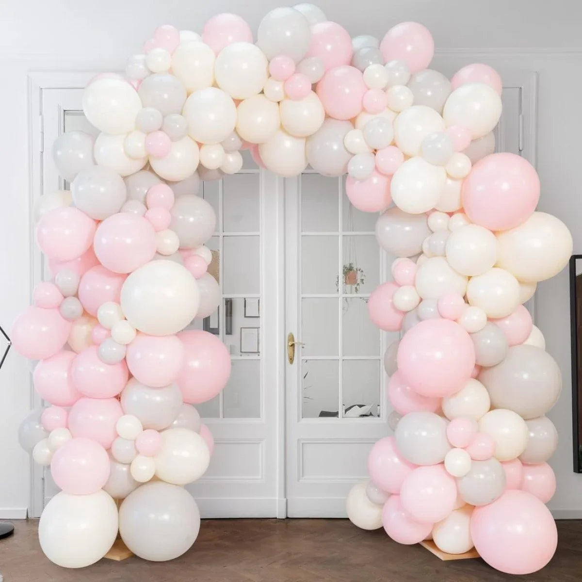 Pink, white, and gray balloon arch decoration set against white double doors indoors