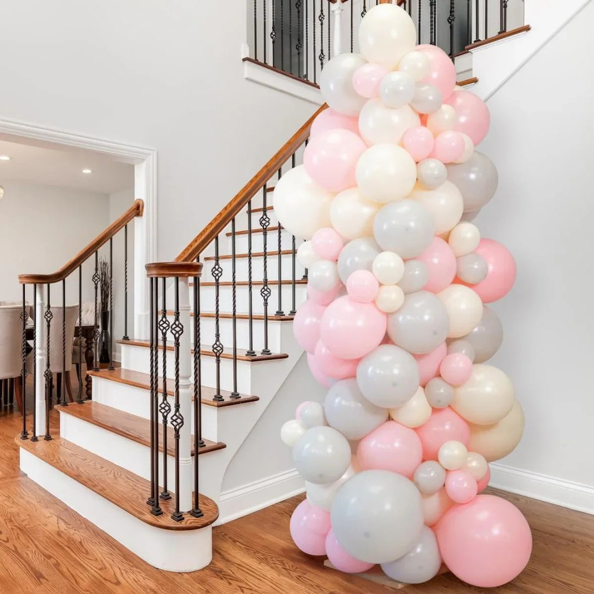Pink, white, and gray balloon pillar decoration next to wooden staircase in modern home