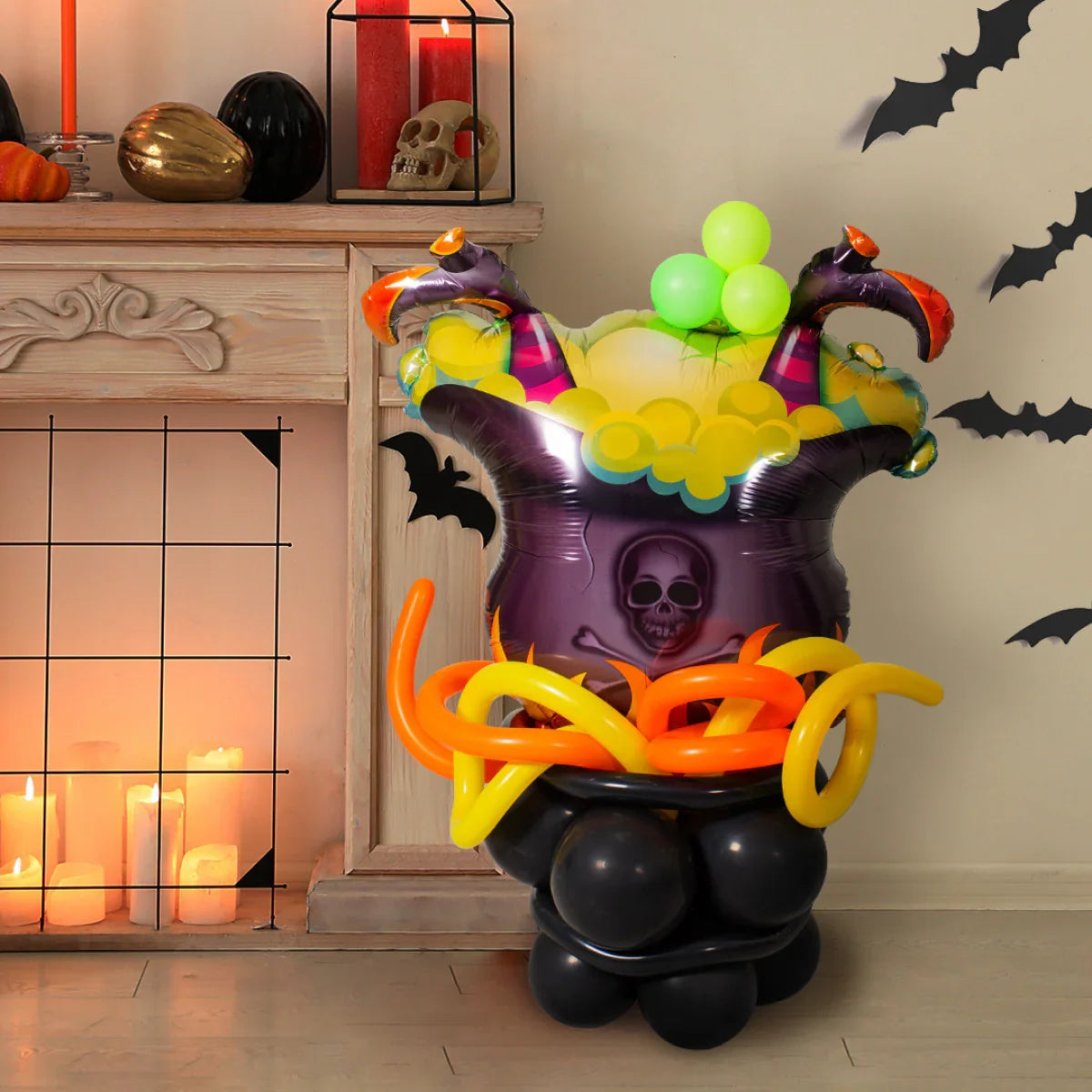 Halloween balloon decoration shaped like a bubbling witch's cauldron with green, yellow, and orange balloons near a candlelit fireplace and black bat wall decals