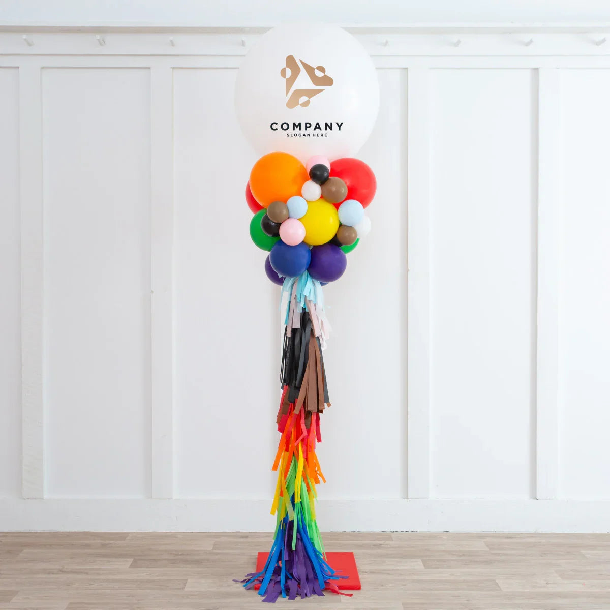 Colorful balloon garland display with tassels and large branded white balloon against white paneled wall