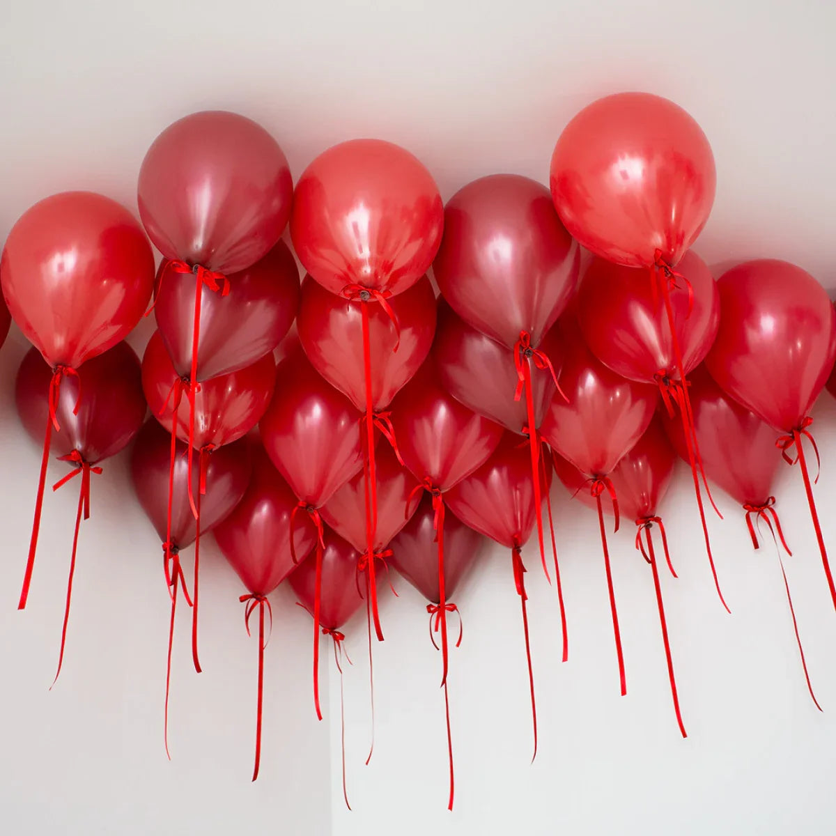 Cluster of dark cherry red helium balloons tied with red ribbons on a white ceiling