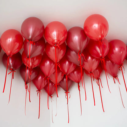 Cluster of dark cherry red helium balloons tied with red ribbons on a white ceiling