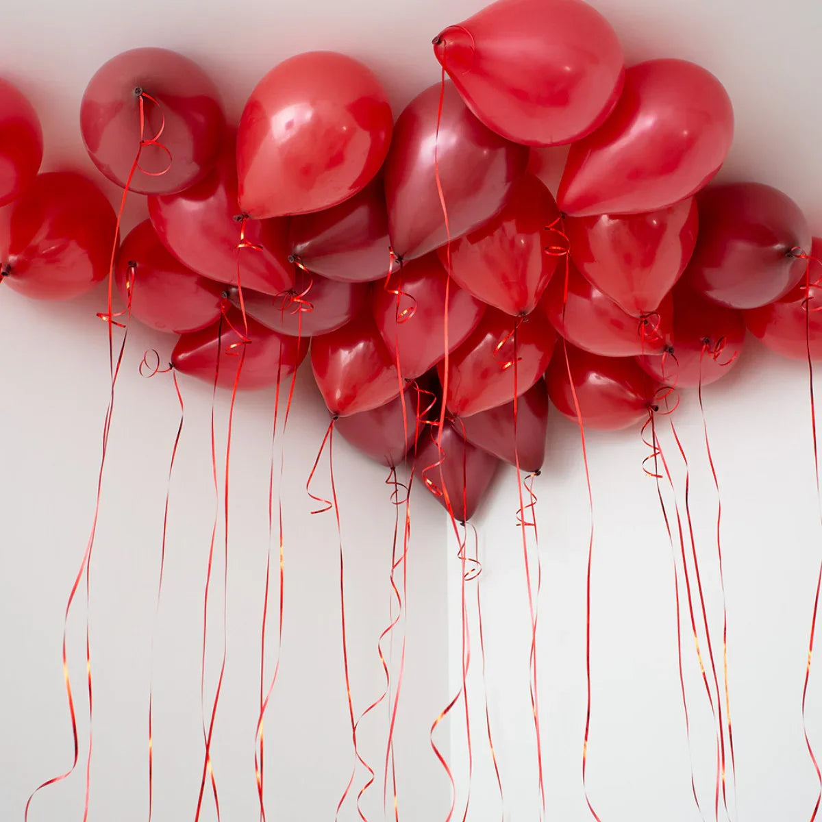 Cluster of dark cherry red helium balloons with ribbons floating against a white ceiling