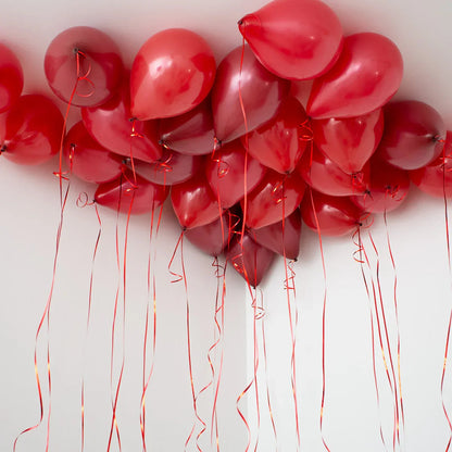 Cluster of dark cherry red helium balloons with ribbons floating against a white ceiling
