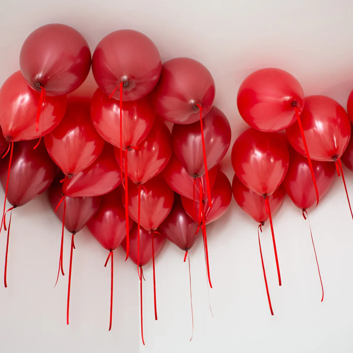 Cluster of dark cherry red helium balloons floating on a white ceiling with red ribbons