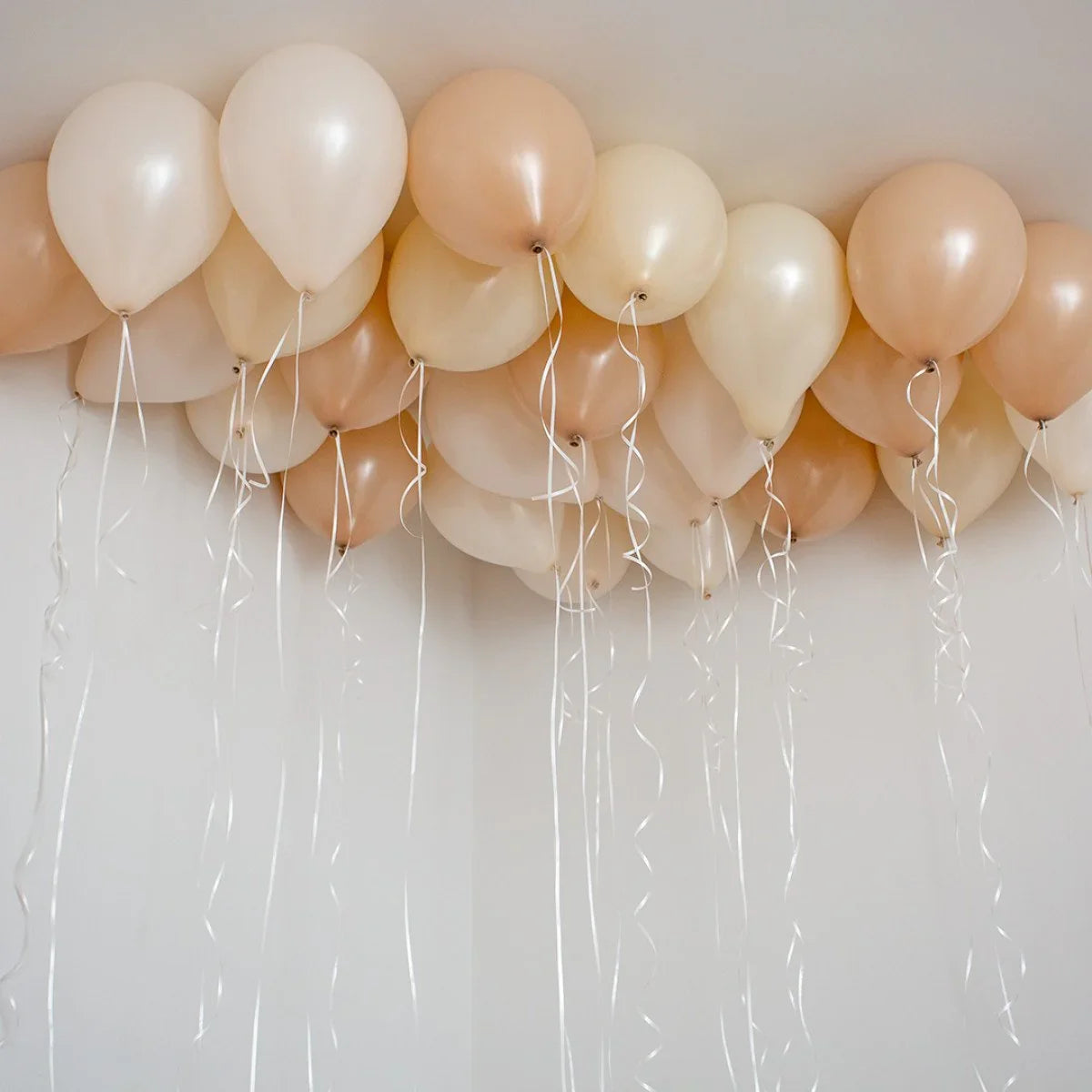 Neutral beige and cream helium balloons with curled ribbons floating on white ceiling