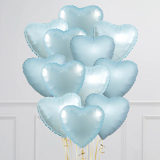 Bunch of shiny baby blue heart-shaped foil balloons with golden ribbons against a white wall