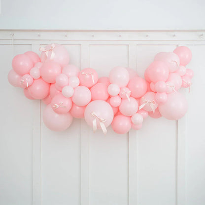 Baby pink and light pink balloon garland with satin bows hanging on white paneled wall