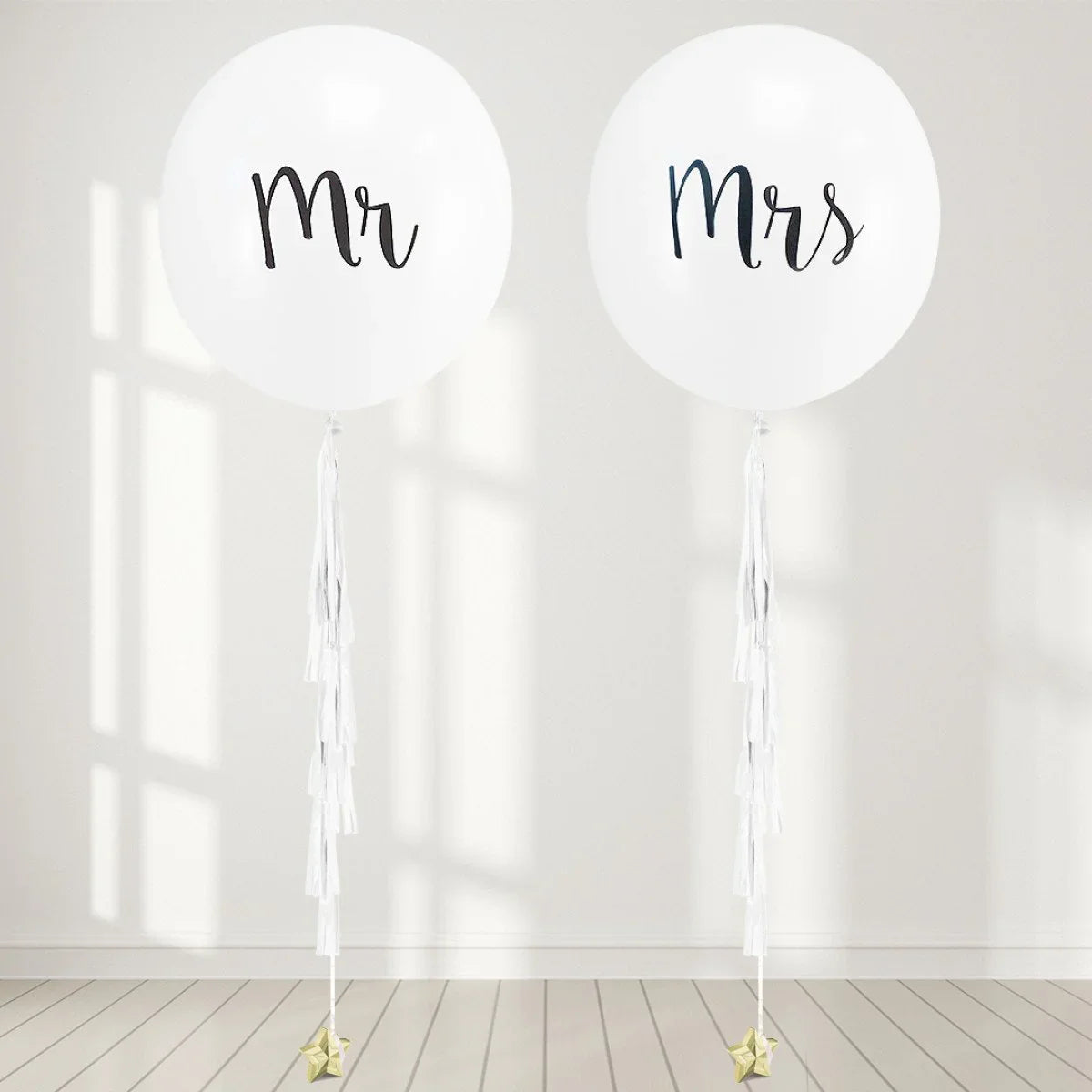 Large white Mr and Mrs balloons with white tassels on light wood floor and wall