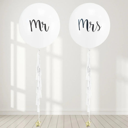 Large white Mr and Mrs balloons with white tassels on light wood floor and wall
