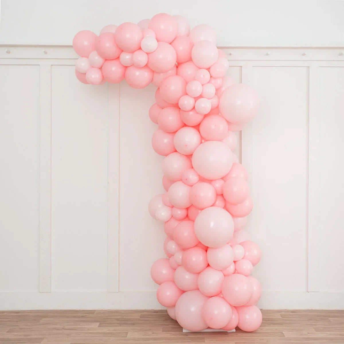 Asymmetric arch made of various sized baby pink balloons against white paneled wall