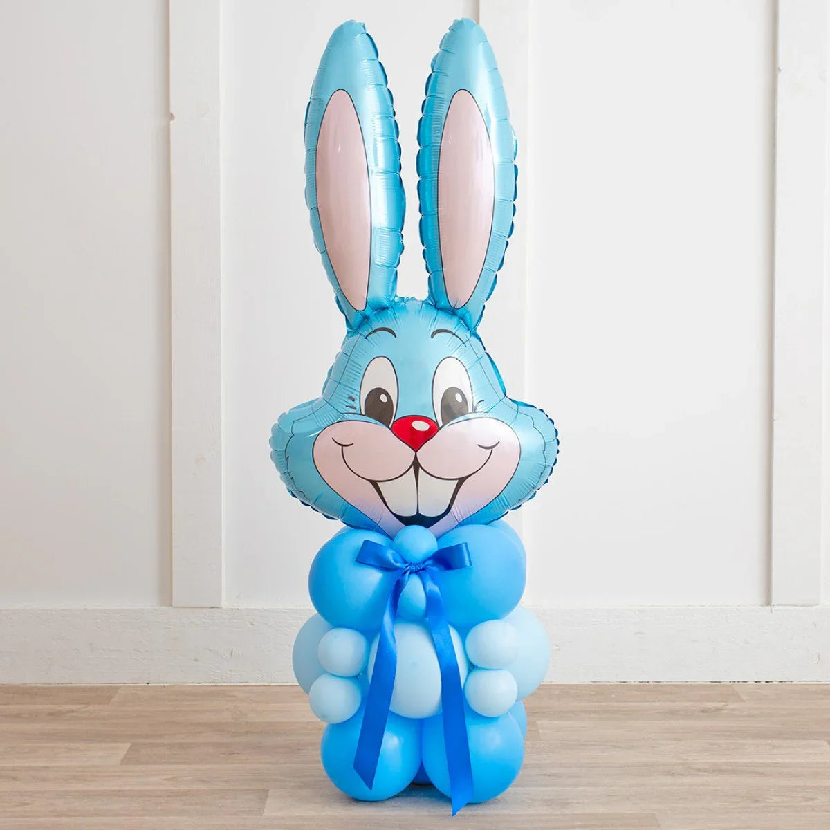 Blue Easter bunny balloon decoration with smiling face, large ears, and blue ribbon bow on wooden floor