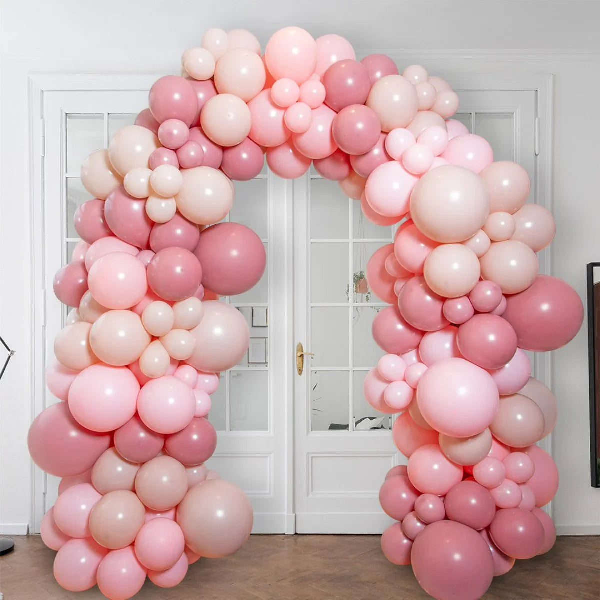 Pink and rose balloon arch decorated with cherry blossom shapes in front of white double doors