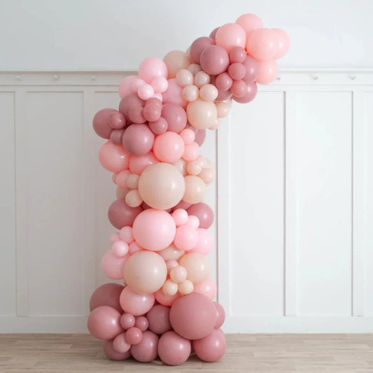 Asymmetric balloon arch with cherry blossom tones in pink and mauve shades against white wall