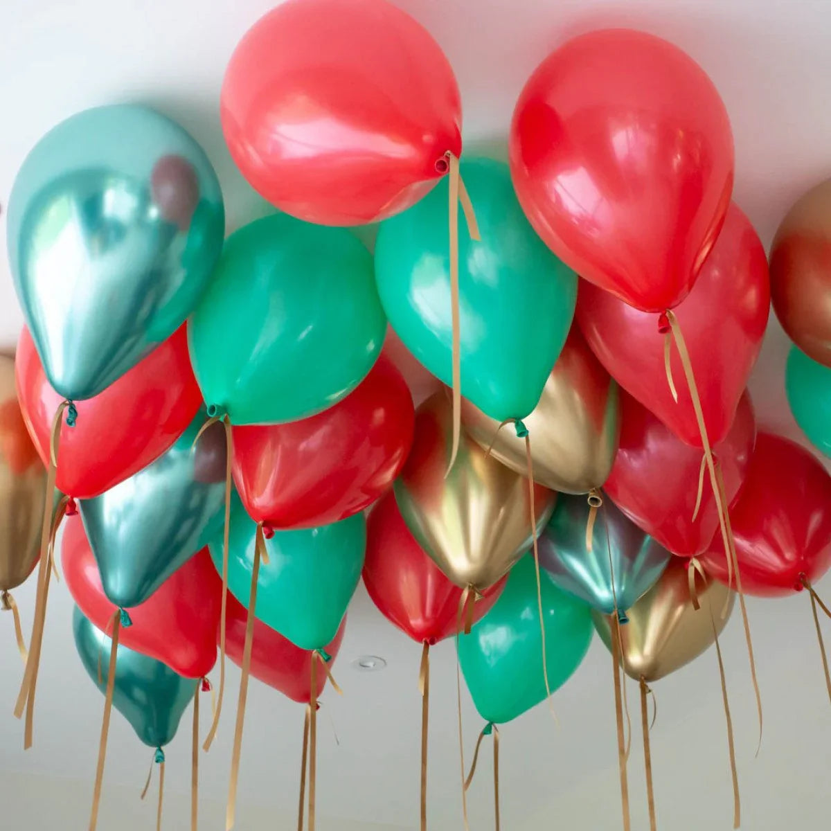 Red, green, blue, and gold helium balloons clustered on a white ceiling for Christmas decoration