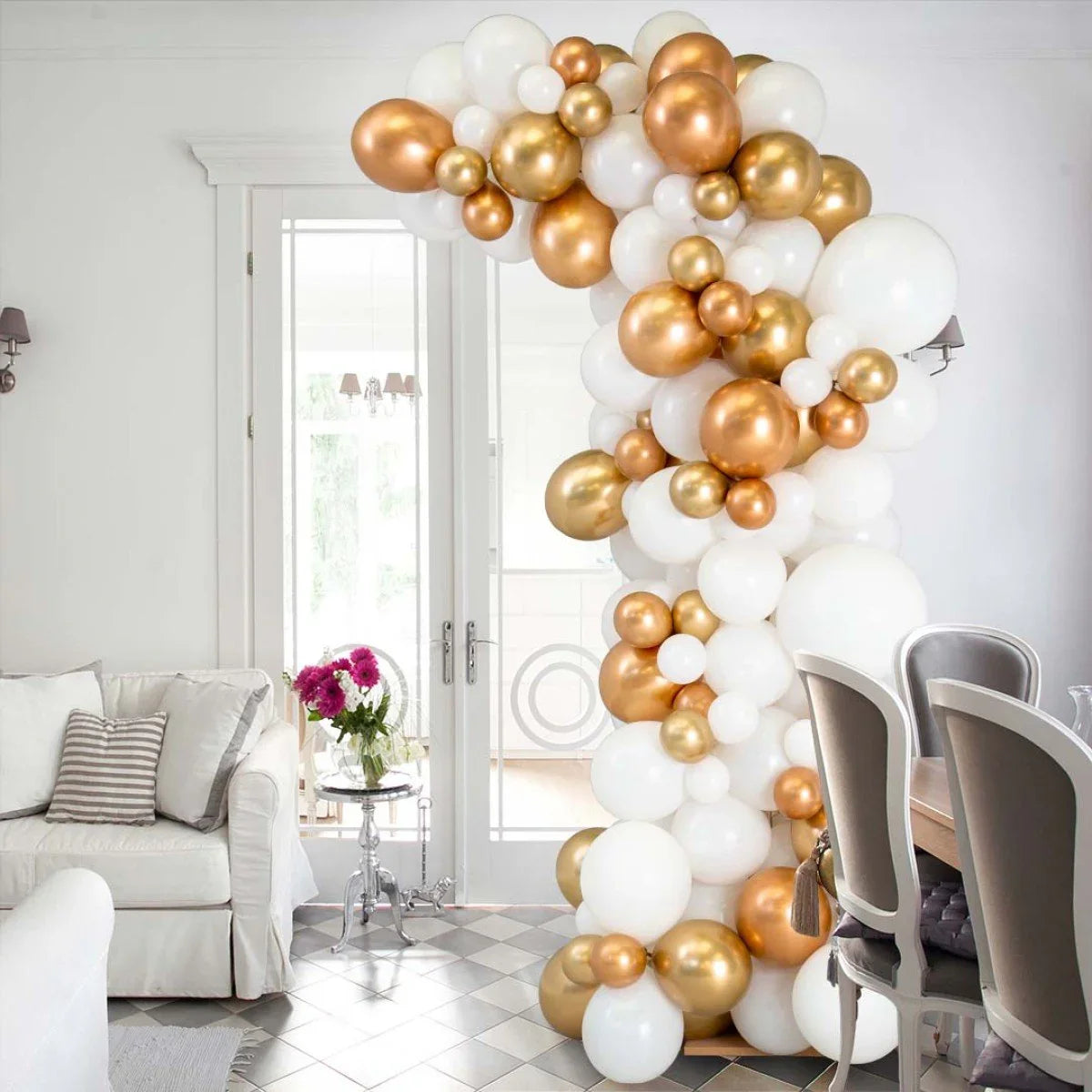 Asymmetric balloon arch in white, gold, and copper inside a bright, elegant living-dining room