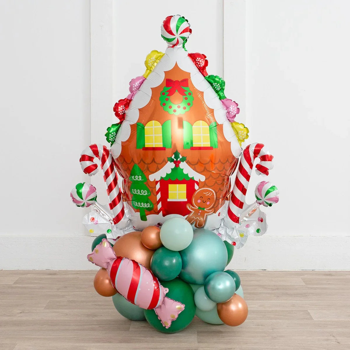 Christmas gingerbread house balloon decoration with colorful candy and green, blue, copper balloons on wood floor