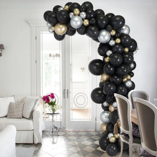 Asymmetric indoor balloon arch with black, gold, and silver balloons in bright living-dining room